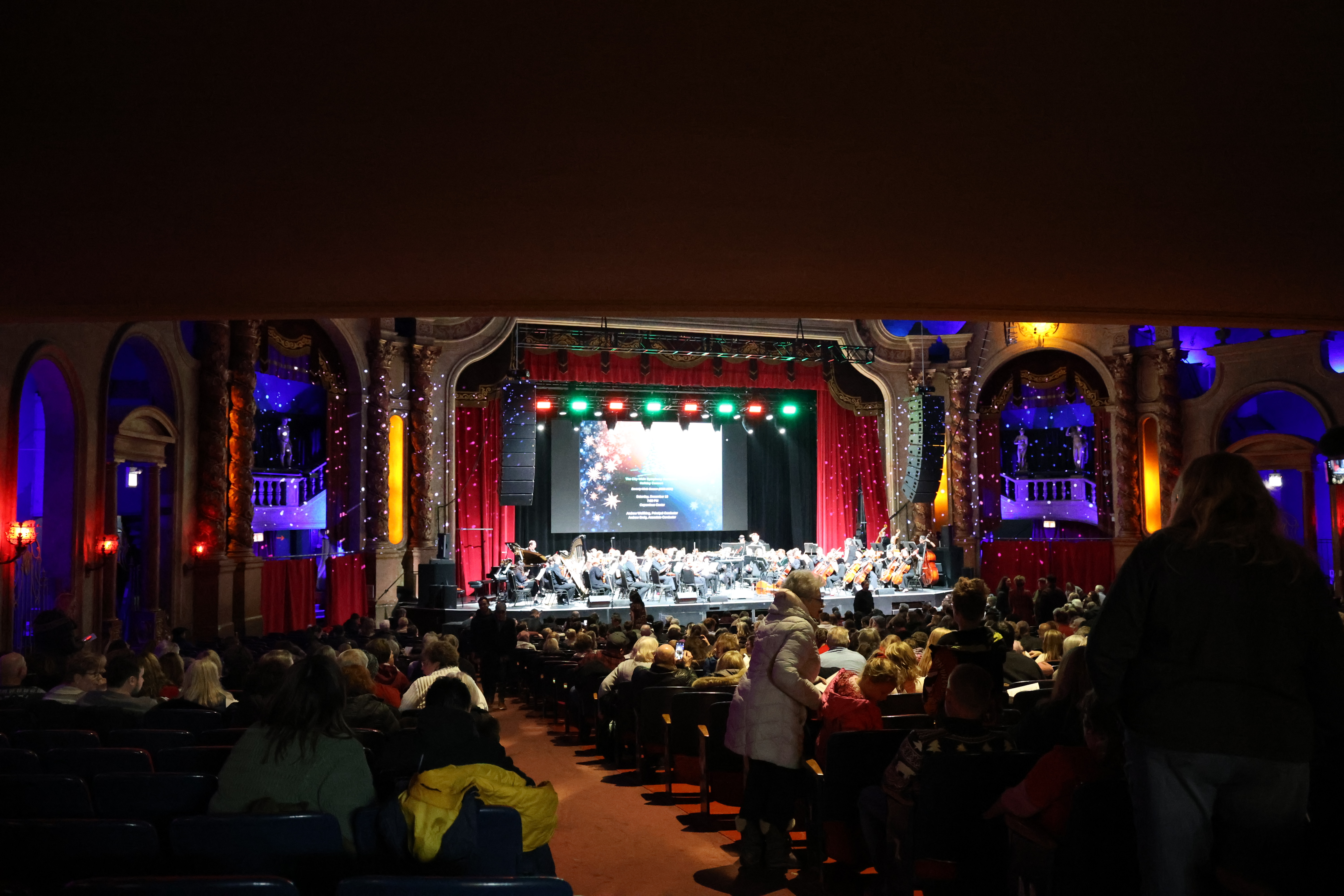 Photograph of a symphony on stage with a seated audience.